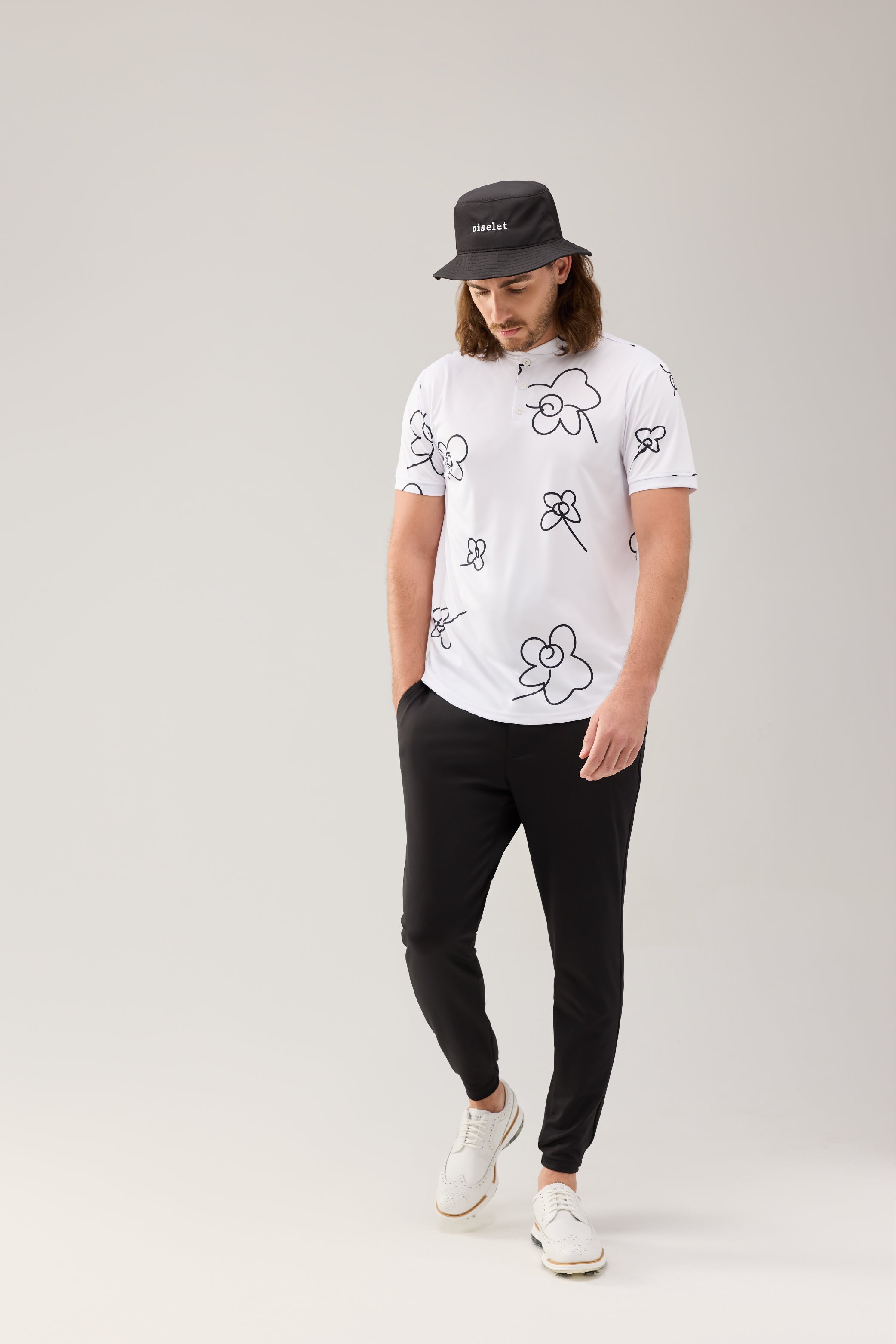 Golfer wearing the Lecolet bucket in black with the word oiselet embroidered on the front, SEED polo Wild Flower white, and STEM Jogger in black