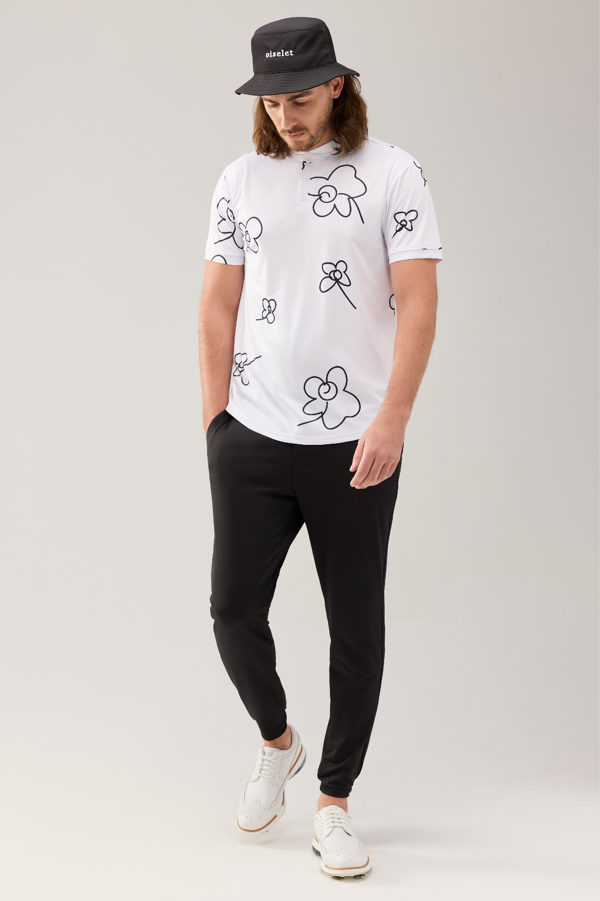 Golfer wearing the Lecolet bucket in black with the word oiselet embroidered on the front, SEED polo Wild Flower white, and STEM Jogger in black